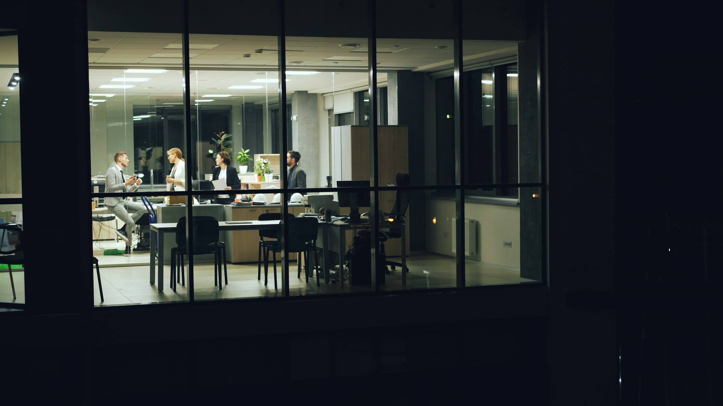 A small team working together in a lit office at night, seen from outside